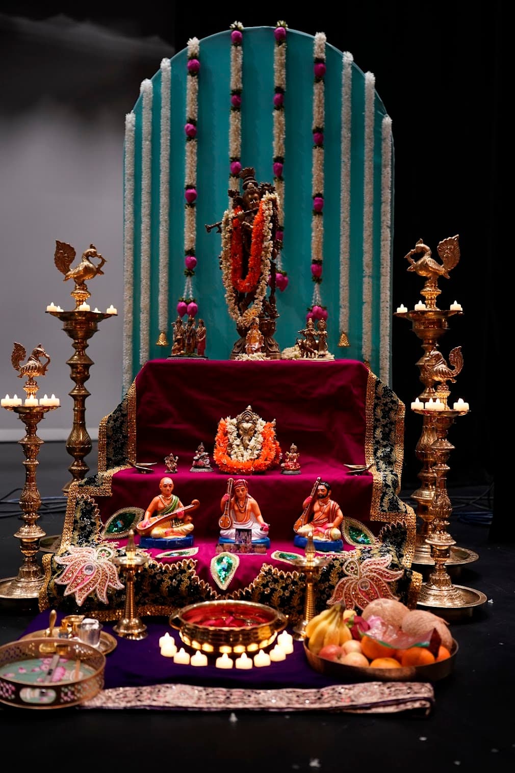 A tiered brass and velvet altar installation flanked by peacock lamps