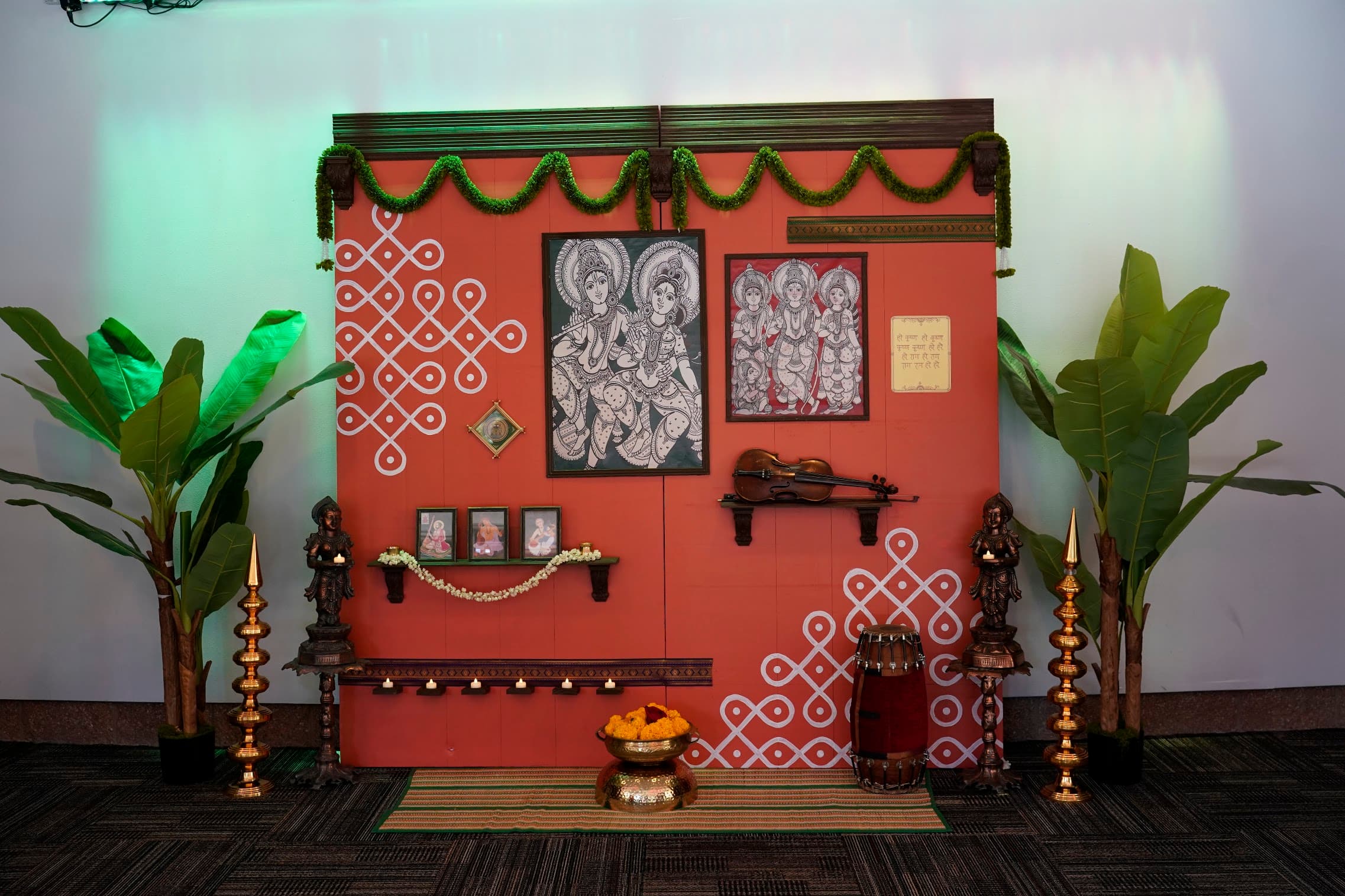 An ochre wall installation with kolam motifs, pichwai art, violin and mridangam
